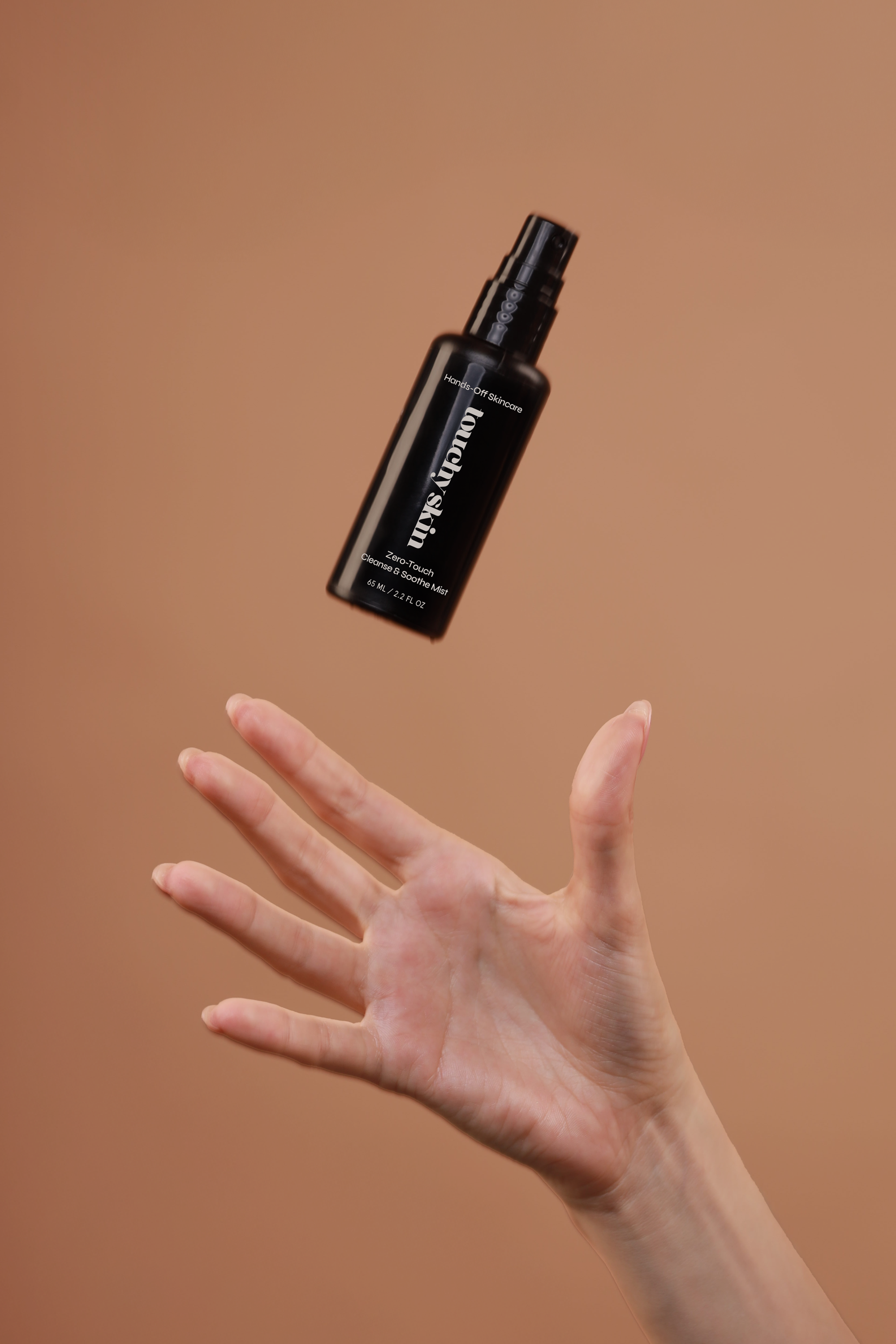 Hand tossing a Touchy Skin Zero-Touch Cleanse & Soothe Mist bottle against a warm beige background, captured mid-air.